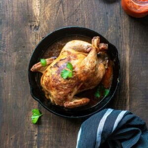 Whole cooked chicken in cast iron pan with garnish