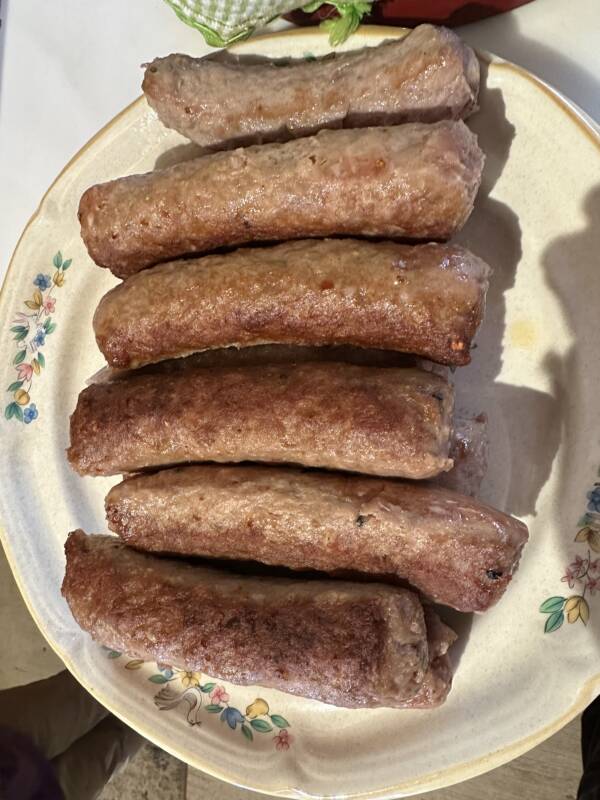 Six savory sausage links on a white plate with a fork.